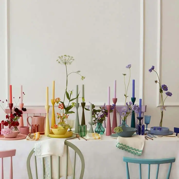 Vibrant dining table decor with colorful candles, vases, and fresh flowers for a casual setting.