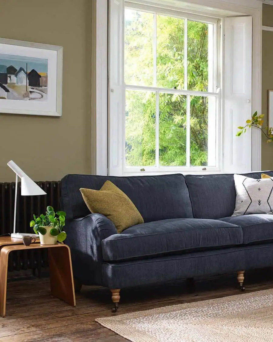 Living room with a dark grey sofa, green cushions, wooden side table, and large window view.