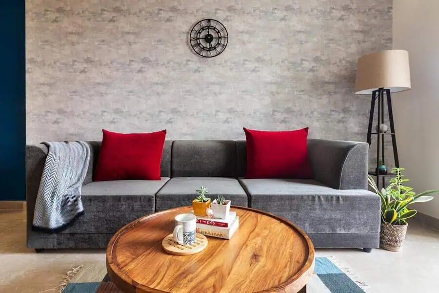 Dark grey sofa with red cushions, wooden coffee table, textured wall, and decorative plants.