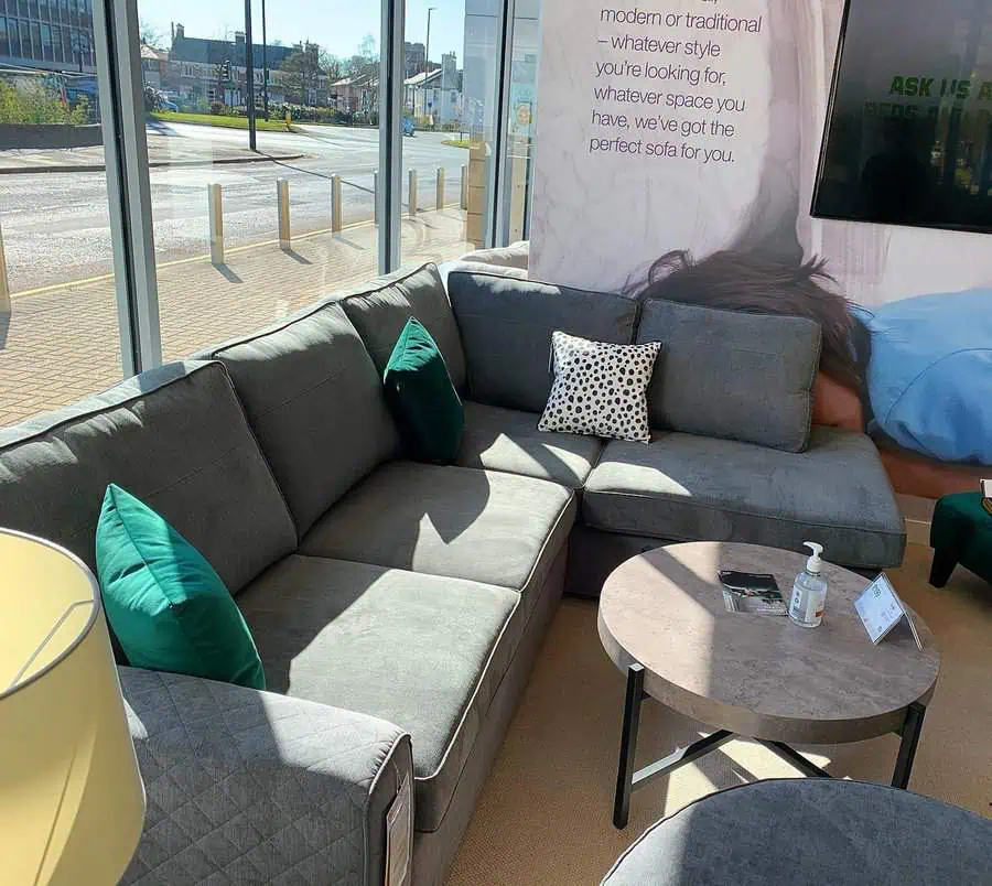 Dark grey sectional sofa with green and patterned cushions, round coffee table, and large windows.