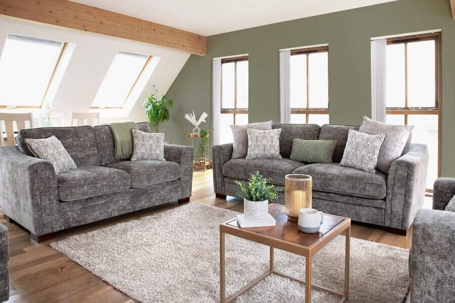 Dark grey sofas with patterned cushions, green accent wall, wooden floors, and cozy decor elements.