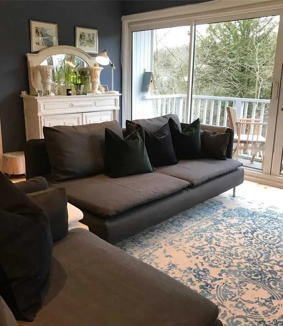 Dark grey sofa with green cushions, blue accent wall, vintage white cabinet, and patterned rug.