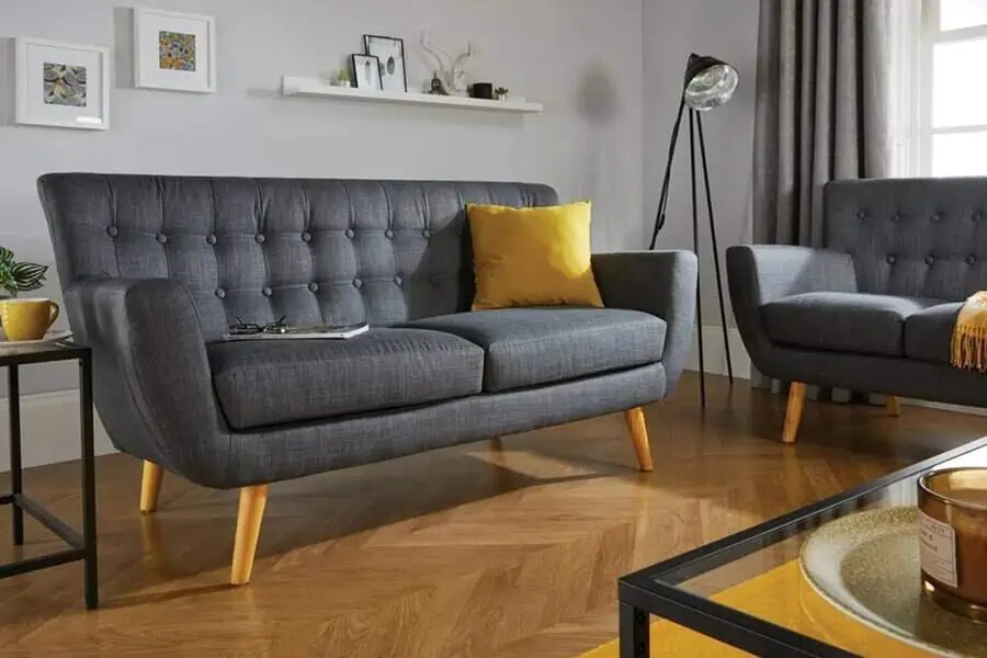 Dark grey tufted sofa with yellow accents, wooden legs, and modern decor on wooden flooring.