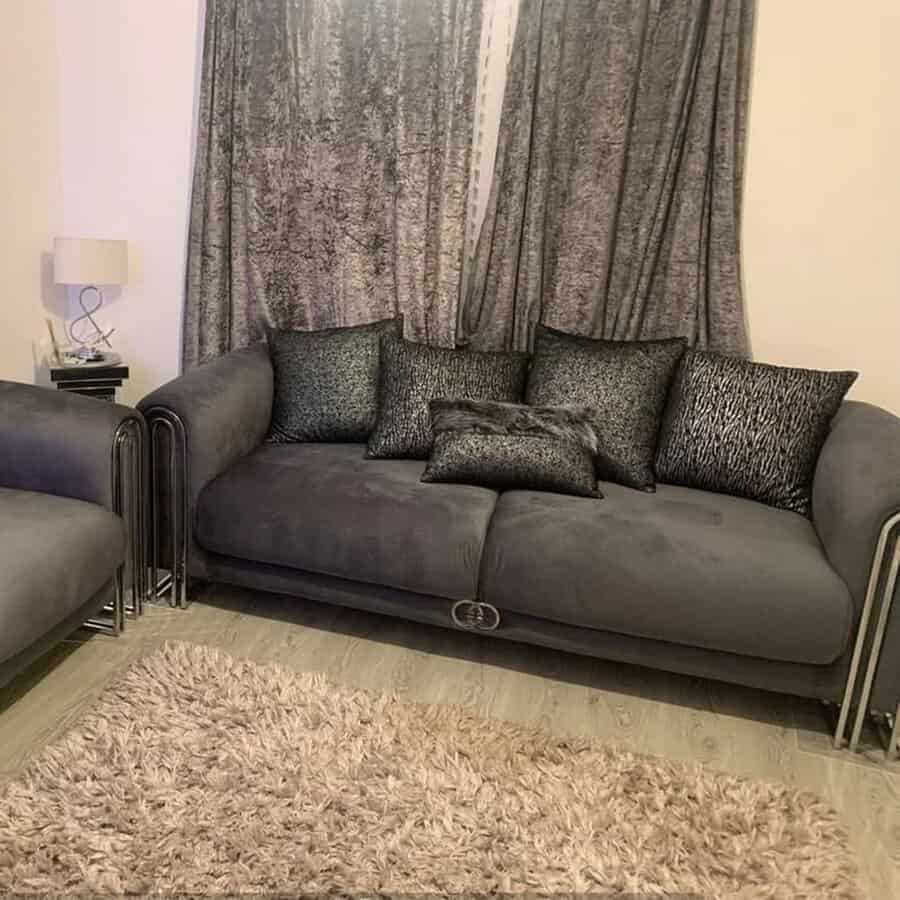 Cozy living room with a dark grey sofa, matching cushions, velvet curtains, and a shaggy rug.