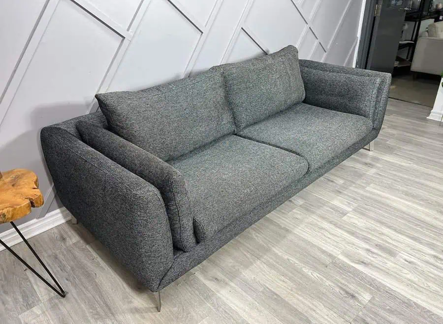 Dark grey modern sofa with sleek design, wooden side table, and geometric accent wall.