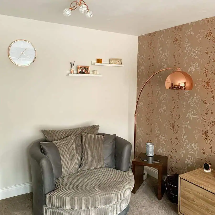 Dark grey round sofa with textured cushions, copper floor lamp, and beige patterned wallpaper.