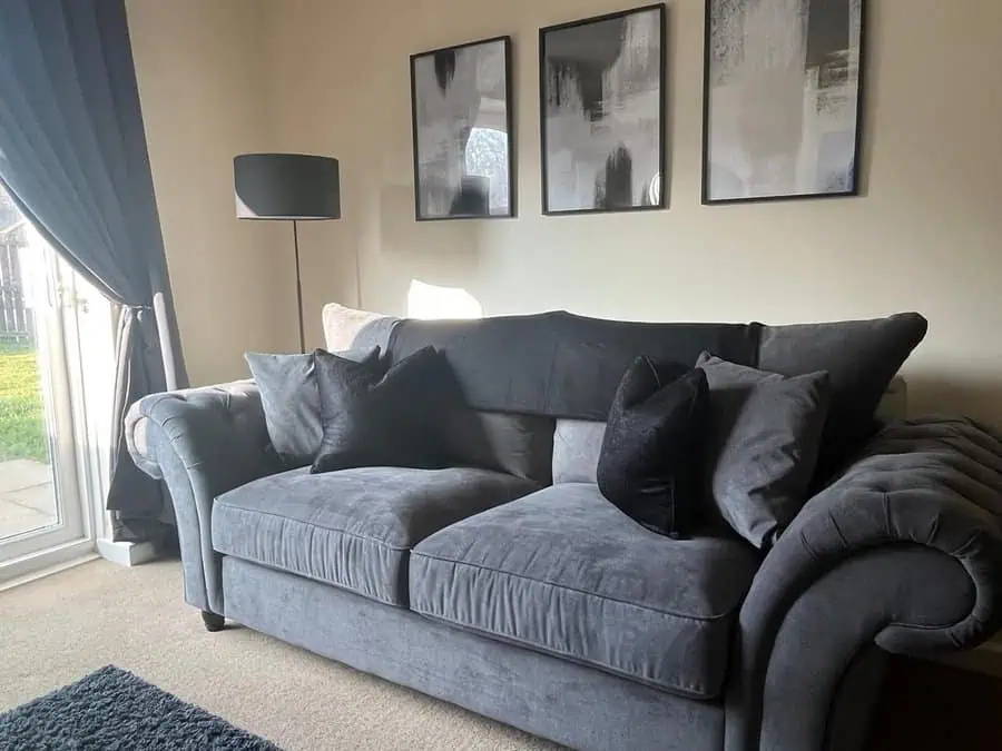 Modern living room with a dark grey sofa, black and grey cushions, abstract wall art, and natural light.