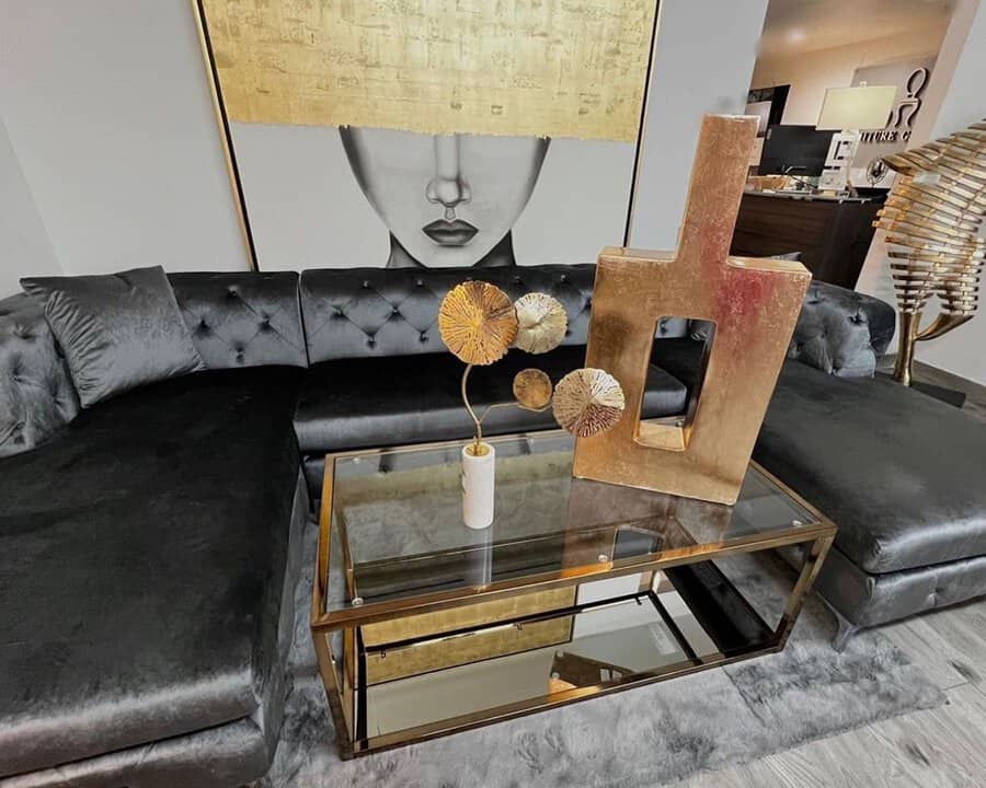 Dark grey tufted sofa paired with luxurious gold decor and a glass coffee table.