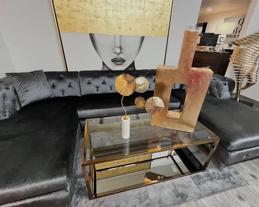 Dark grey tufted sofa paired with luxurious gold decor and a glass coffee table.