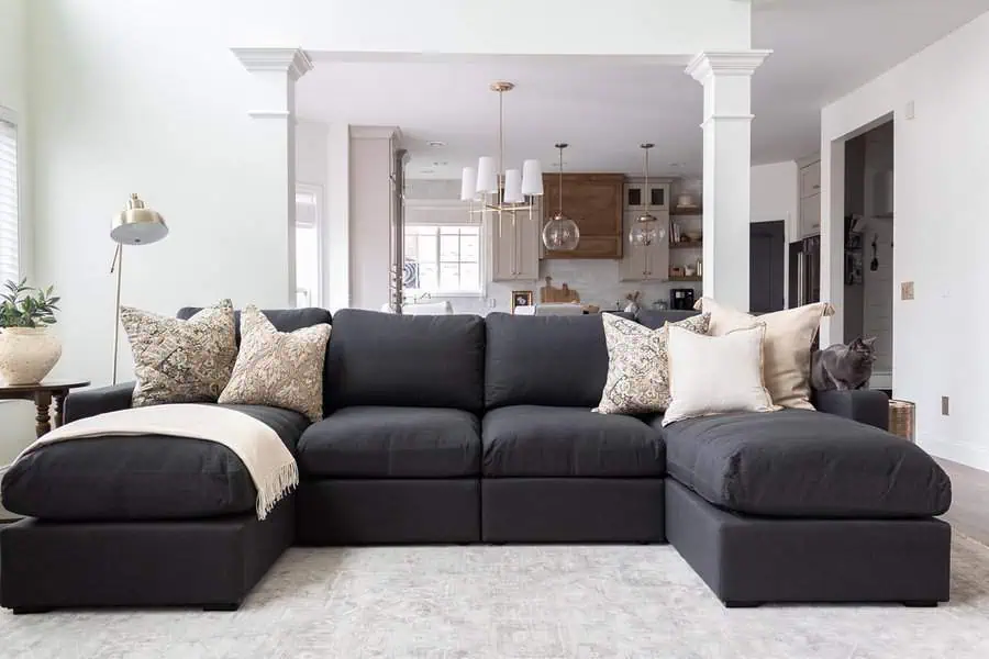 Modern dark grey sectional sofa adorned with elegant patterned and neutral cushions, set in an open-concept living and kitchen area.