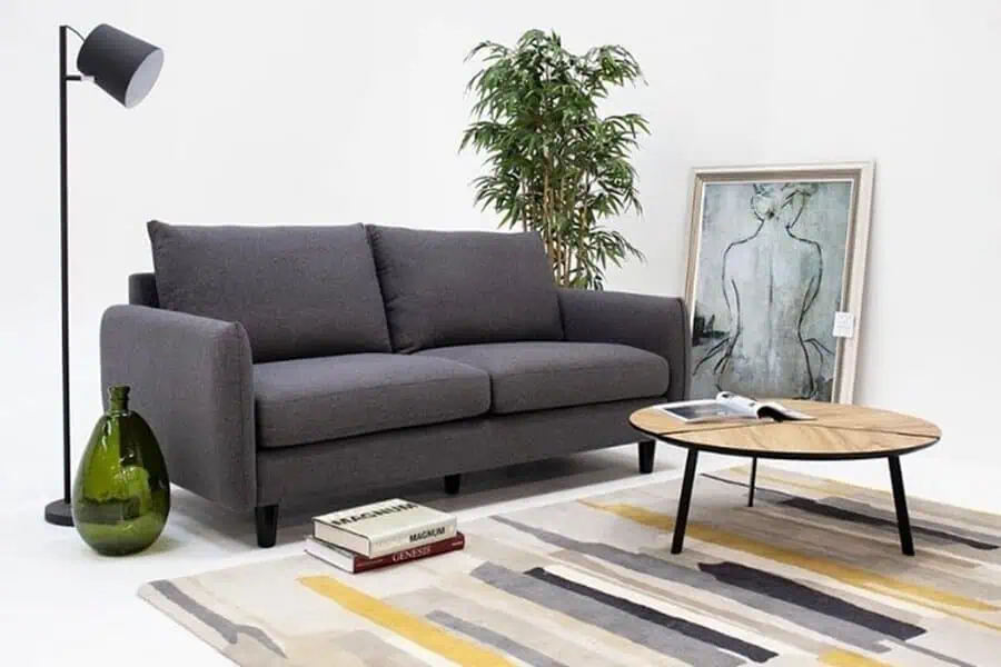 Minimalist dark grey sofa paired with a modern wooden coffee table, abstract rug, and artistic decor.