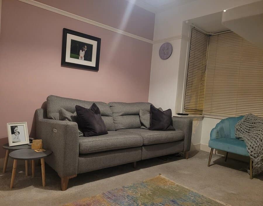 Dark grey sofa with black pillows, pink wall, teal armchair, and light neutral decor accents.