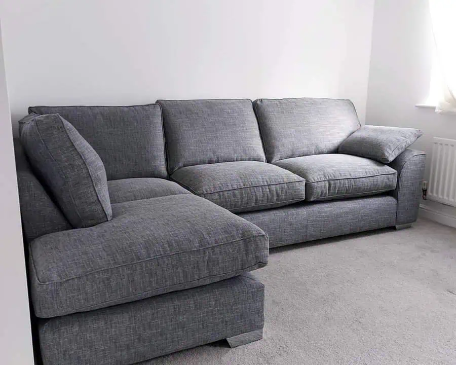 Dark grey sectional sofa in a minimalist white room with soft natural lighting.