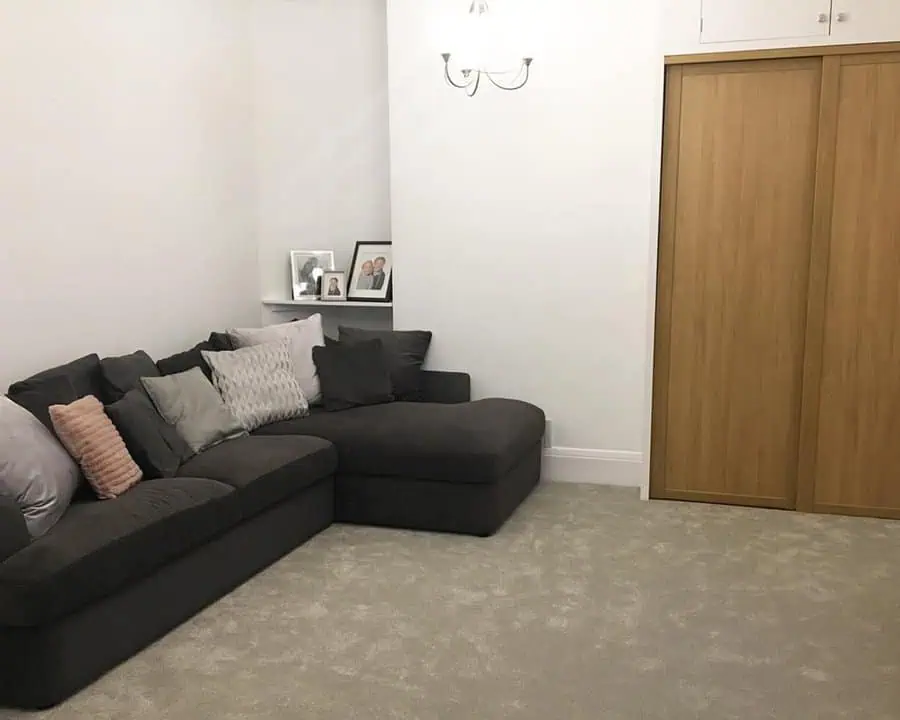 Dark grey sectional sofa with mixed cushions, white walls, and a wooden wardrobe in a cozy room.