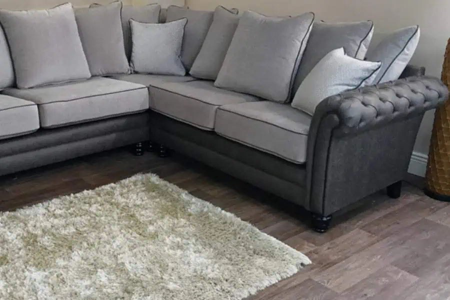 Dark grey Chesterfield-style sofa with light grey cushions, wooden floor, and a fluffy cream rug.