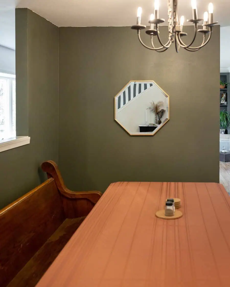 Octagonal mirror on an olive green wall above a wooden bench in a feng shui dining space.