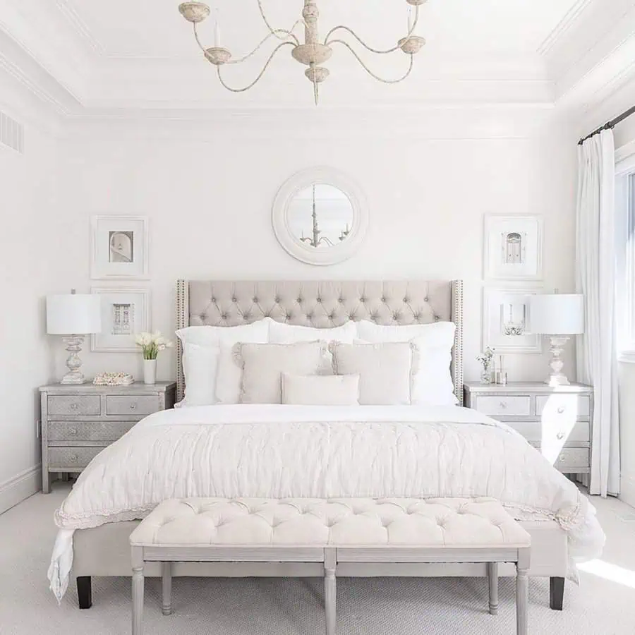 Elegant white bedroom with a round feng shui mirror, tufted bed, and soft neutral decor.