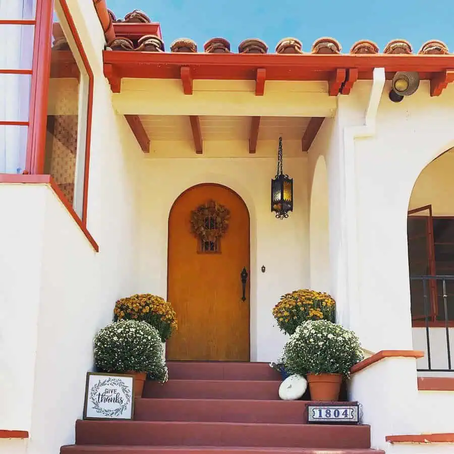 A Spanish-style home with an arched wooden door, terracotta steps, and potted plants.