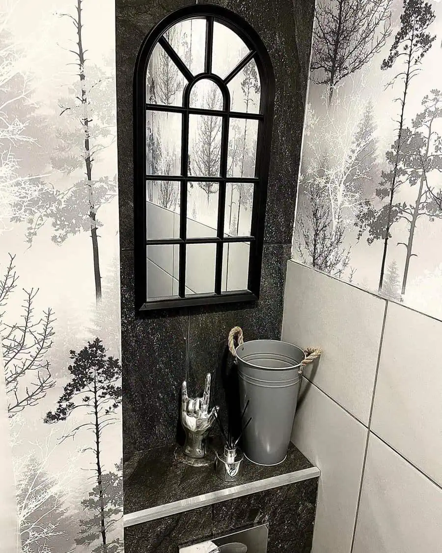 Bathroom with grey and white forest-themed wallpaper, black arched mirror, and decorative accents.