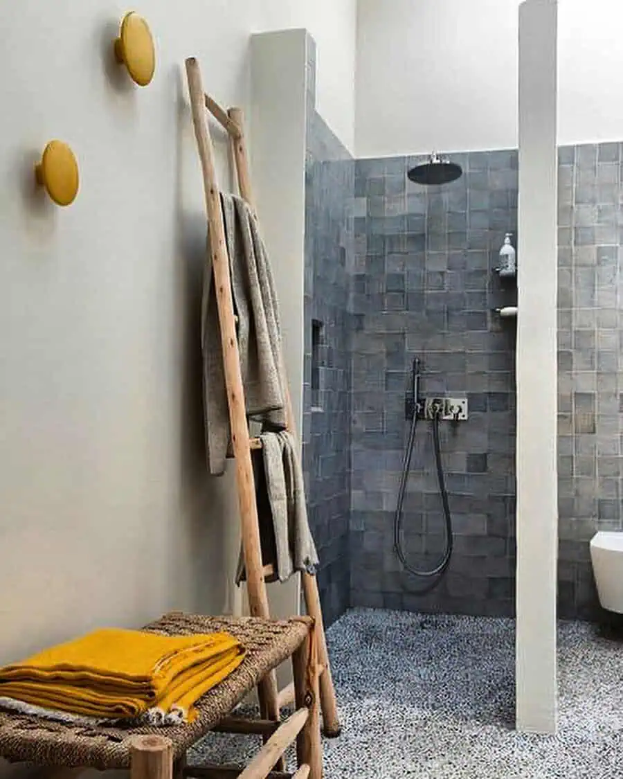 Grey bathroom with small floor tiles, textured shower wall, and rustic wooden ladder decor.