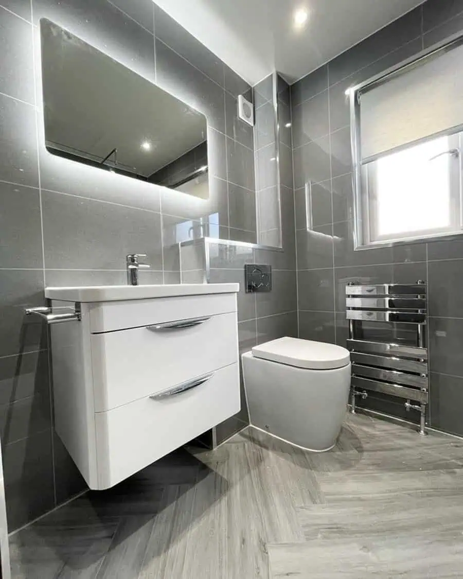 Contemporary grey bathroom with textured flooring, floating vanity, and illuminated mirror.