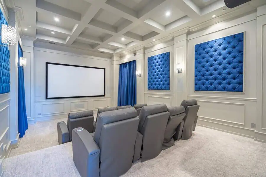 Elegant home theater with luxurious blue tufted panels, cozy reclining chairs, and classic white walls, offering a cinematic experience.