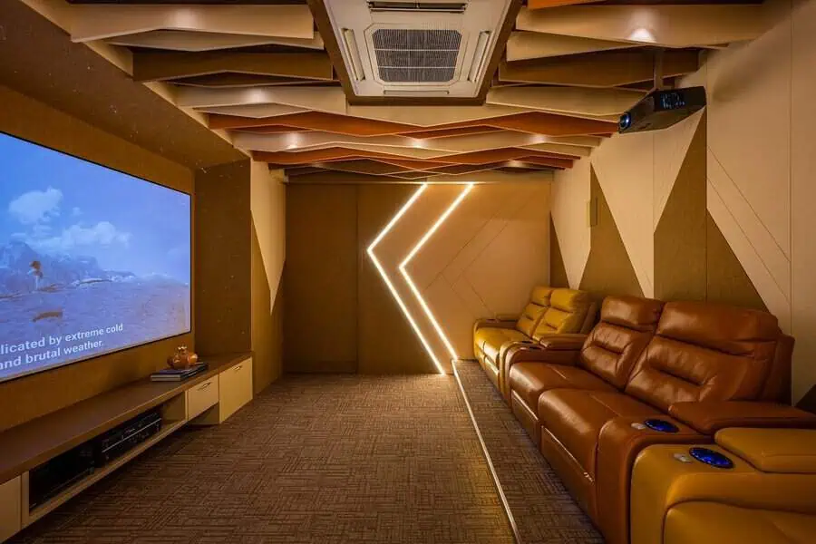 Modern home theater with geometric ceiling panels, warm LED lighting, and leather recliners.