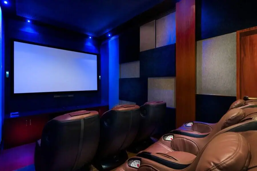 Luxurious home theater with massage recliners, acoustic panels, and dim blue lighting for a cinematic experience.