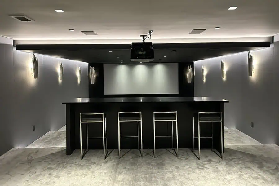 Modern home theater with sleek bar seating, ambient wall lighting, and a minimalist screen setup.