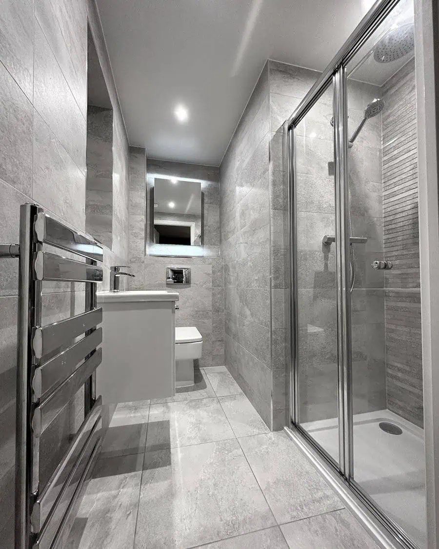 Light grey bathroom with tiled walls and floors, glass shower enclosure, and heated towel rail.