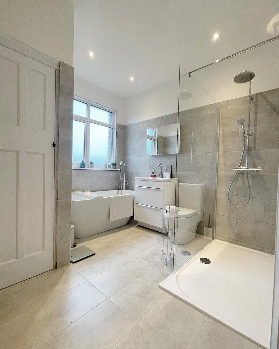 Spacious bathroom with light grey floor tiles, glass shower enclosure, and freestanding tub.