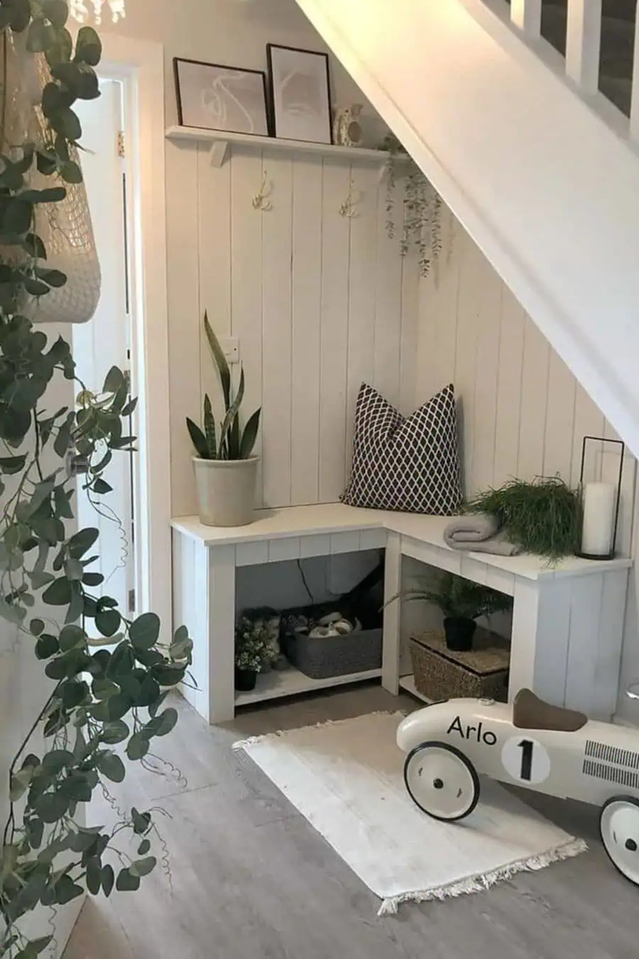 Under-stair corner with white furniture, plants, wall hooks, and a decorative toy car.