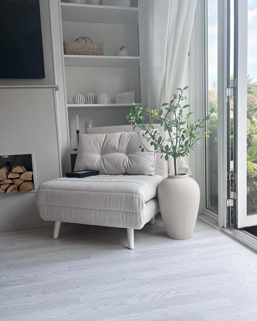 Bright living room corner with a white armchair, bookshelf, large vase, and sliding glass door.