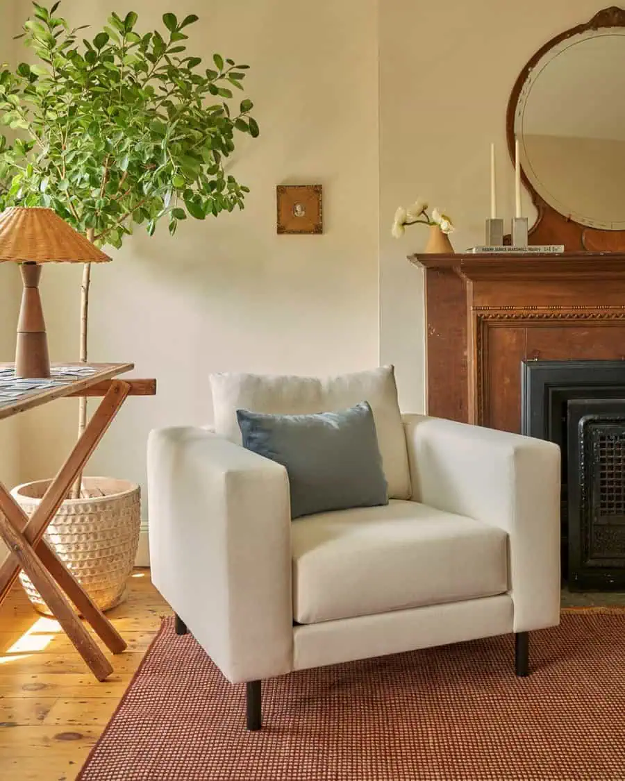 Living room corner with a cream armchair, wooden fireplace, potted plant, and woven basket.