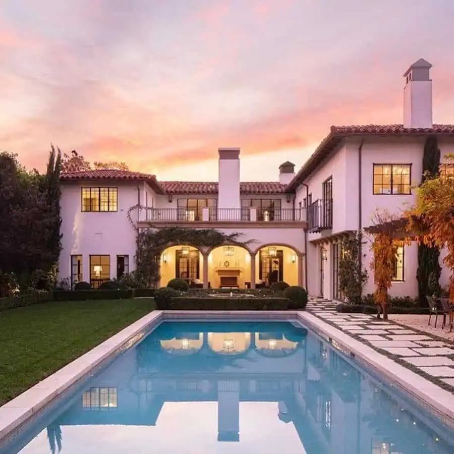 Luxury Spanish-style house with white stucco walls, red tile roof, arches, and a backyard pool.