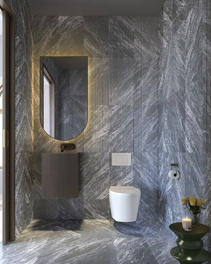 Elegant bathroom with marble-look grey tiles, floating vanity, and illuminated arched mirror.