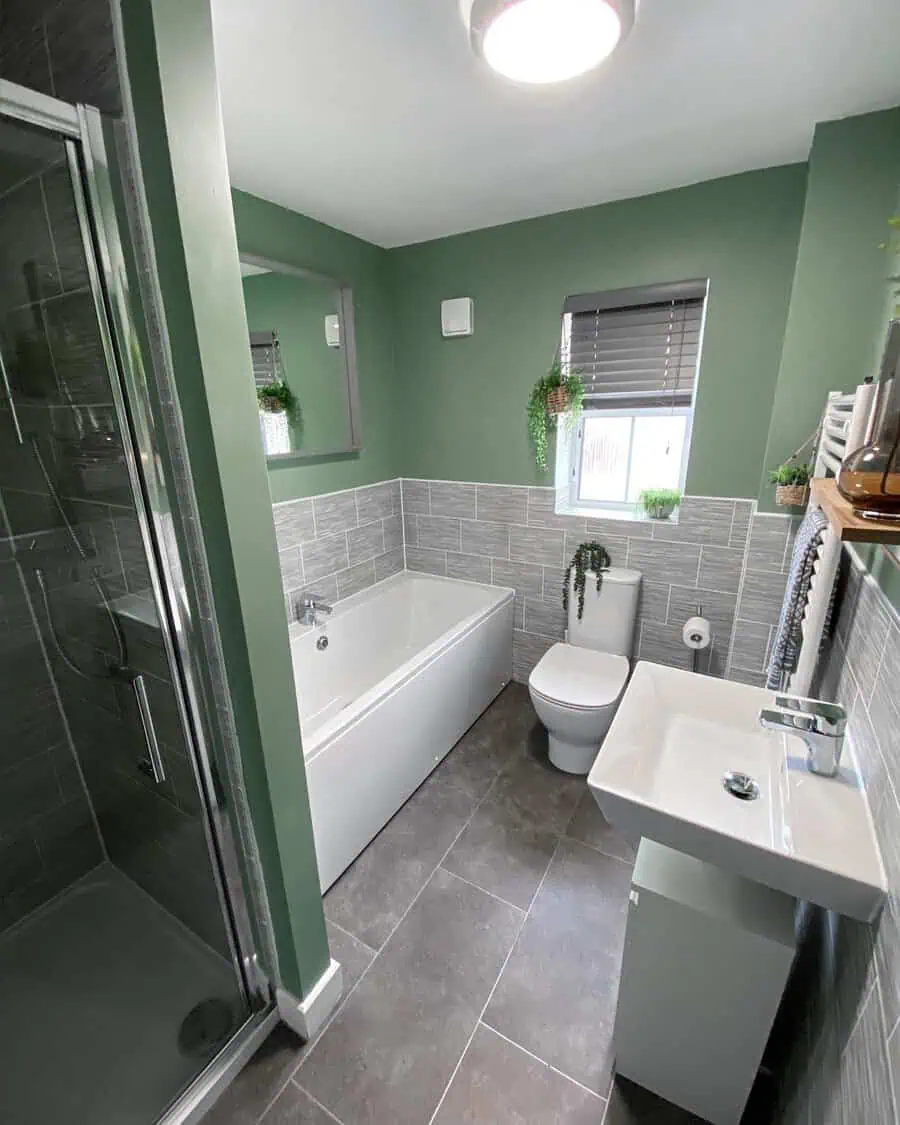 Bathroom with grey floor tiles, green painted walls, white fixtures, and hanging plants.