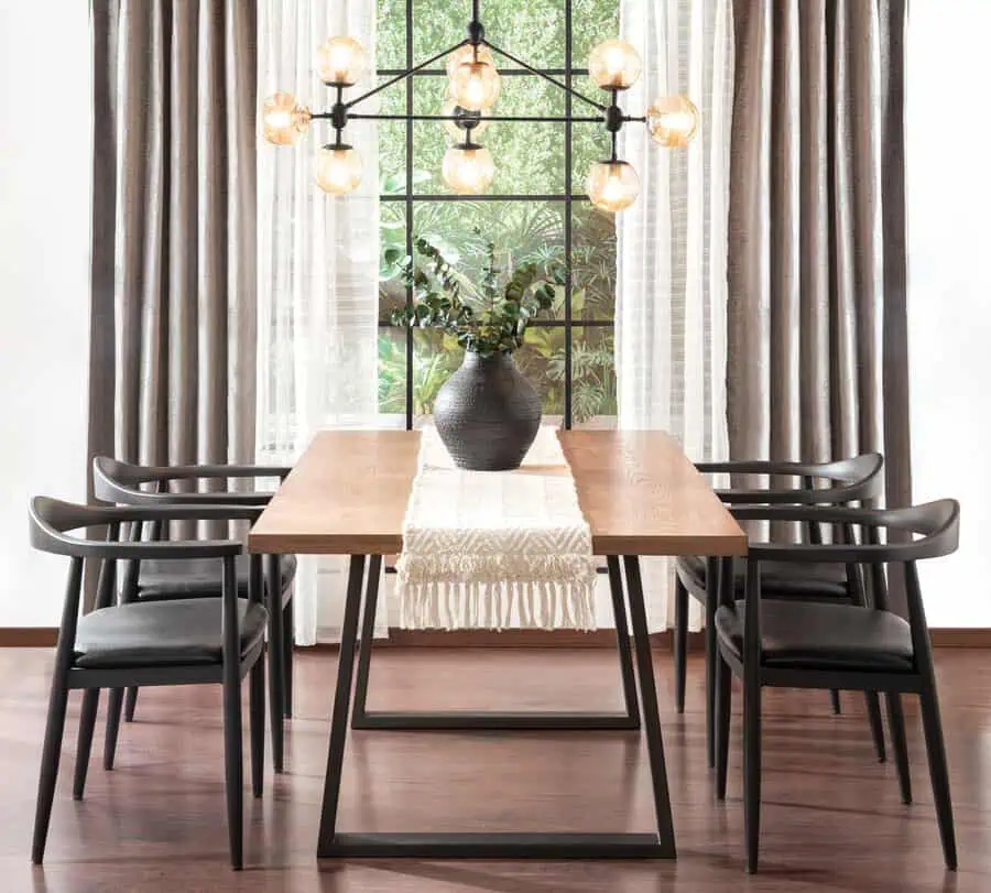 Minimalist dining table with wooden top, black chairs, a textured vase, and modern pendant lighting.