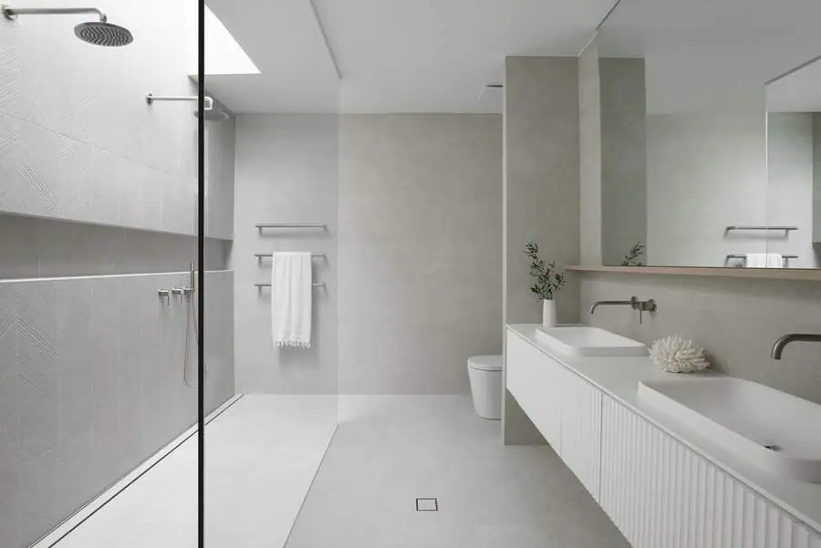 Minimalist bathroom with light grey floor tiles, dual sinks, and a glass walk-in shower.