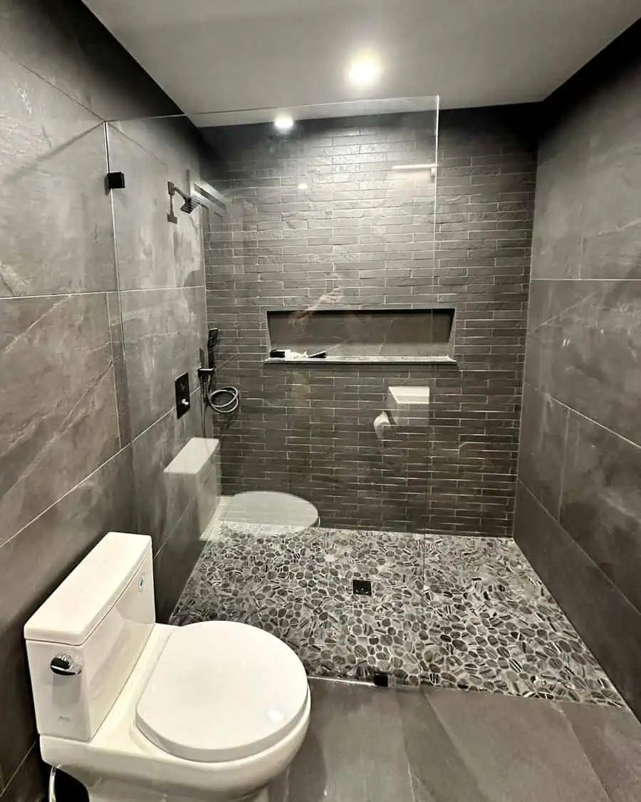 Bathroom featuring dark grey tiles with a mosaic pebble design on the shower floor.