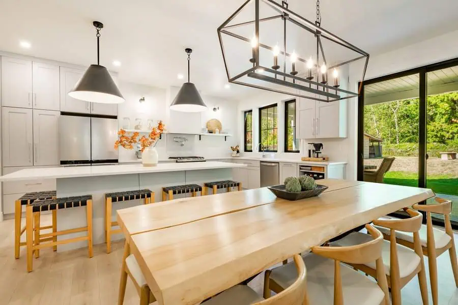 Modern kitchen with natural wood dining table, pendant lighting, and large glass doors.