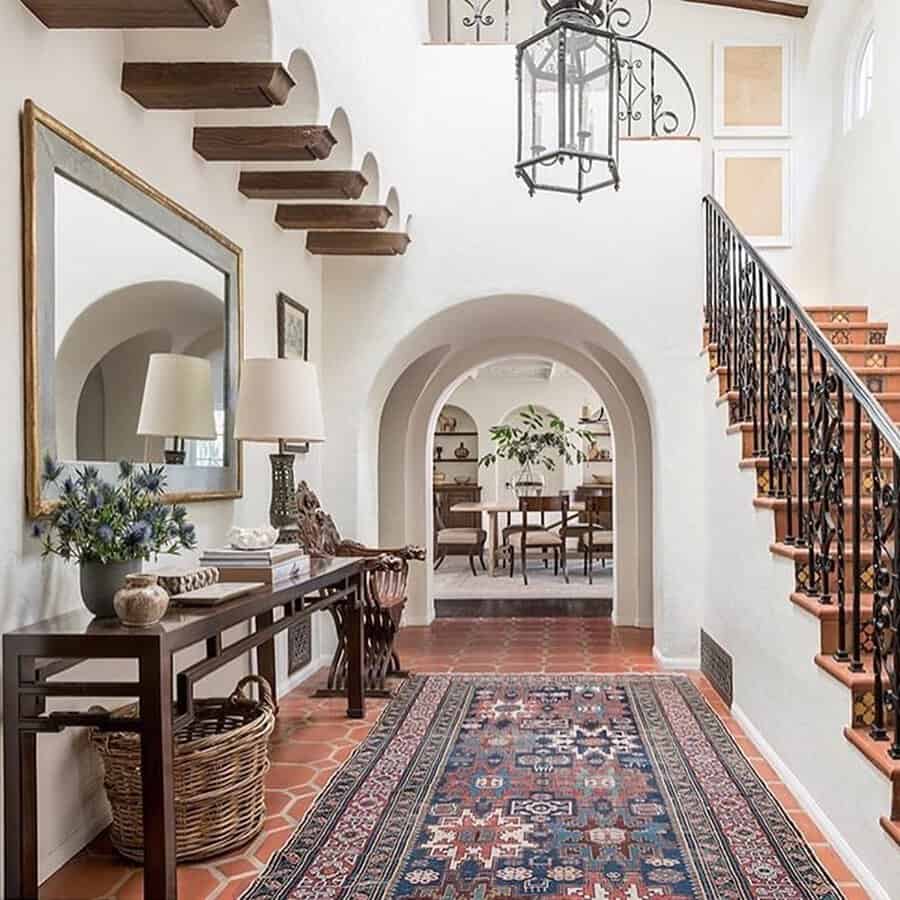 A rustic modern Spanish-style home featuring terracotta floors, arched doorways, and a wrought-iron staircase.