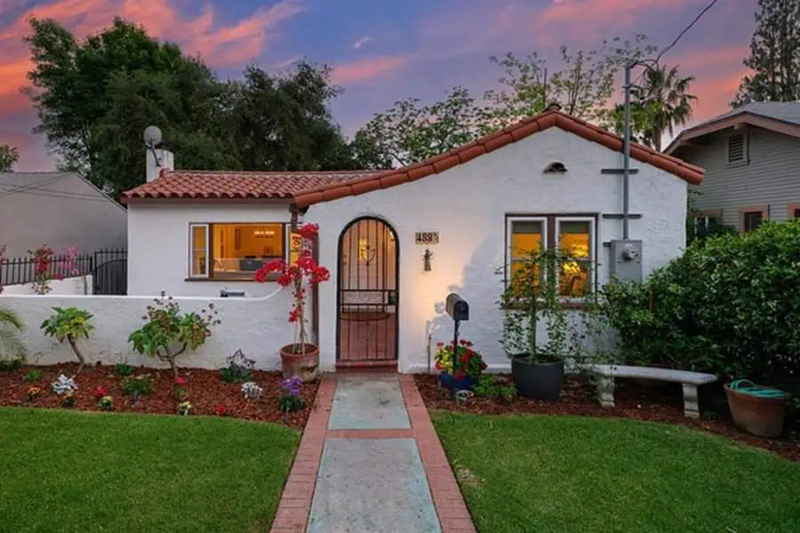 Spanish-style house with white stucco walls, red tile roof, arched doorway, and small garden.