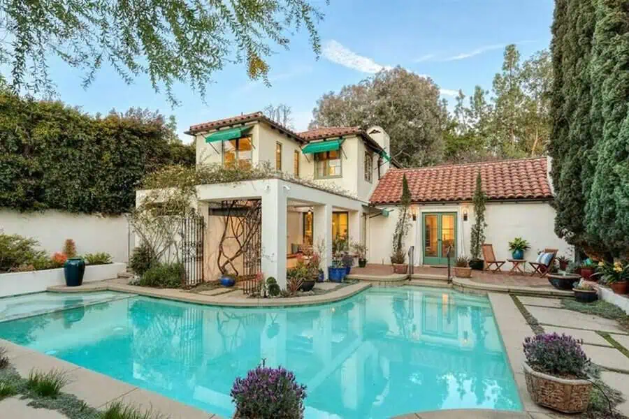 Colonial Spanish-style home with a red tile roof, green awnings, backyard patio, and swimming pool.