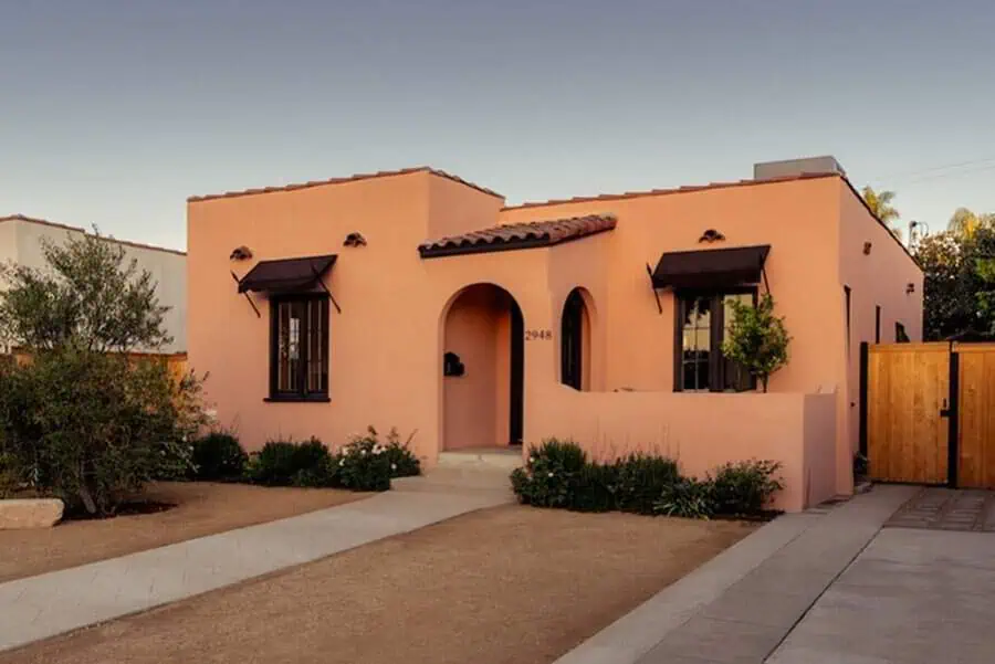 Ranch-style Spanish home with peach walls, red tile roof, arched entryway, and black window awnings.