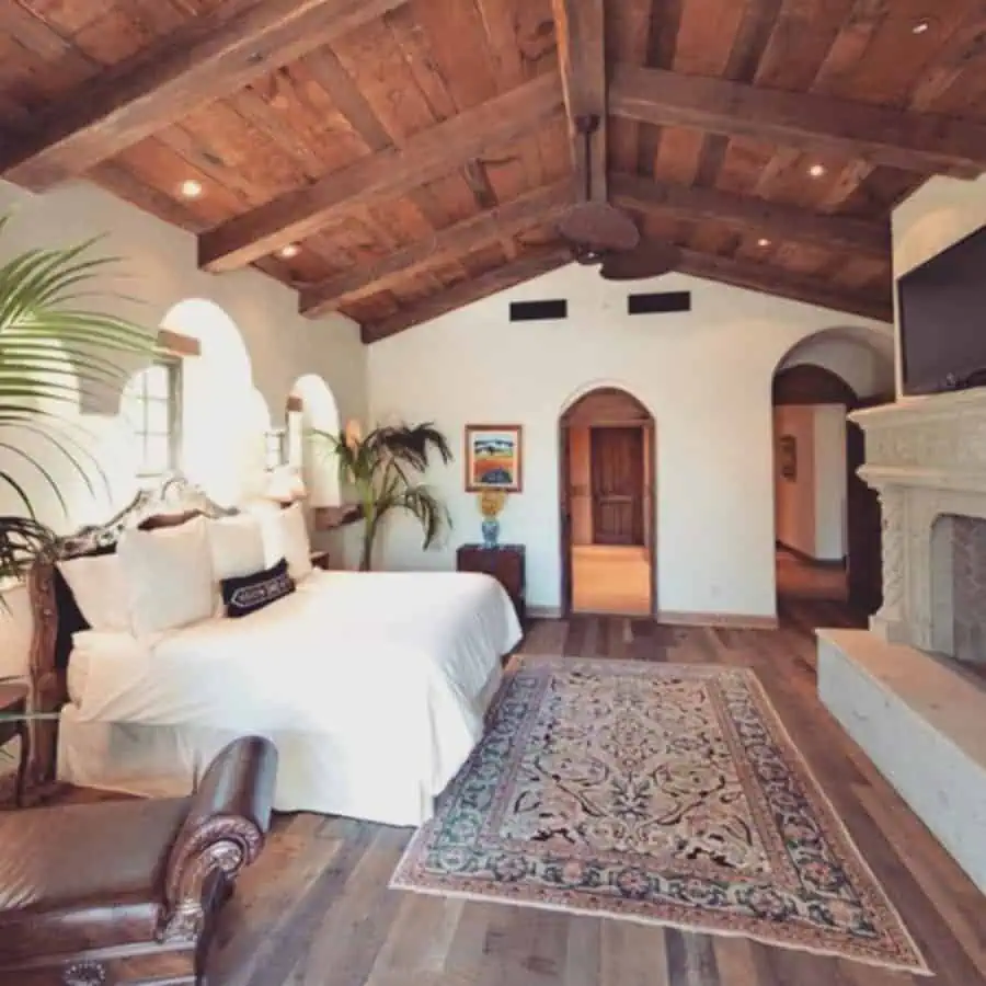 Spanish-style bedroom with a vaulted wooden ceiling, arched doorways, and a decorative fireplace.