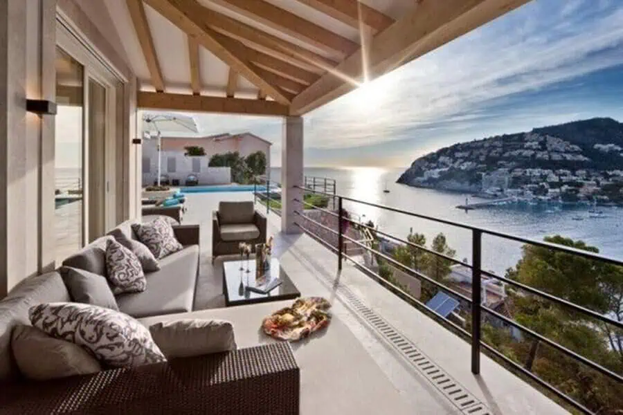 Balcony with wooden beams, outdoor furniture, and panoramic views of the ocean and hills.