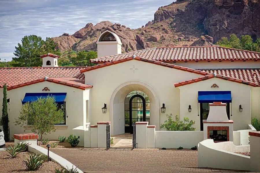 The Spanish-style home showcases red tile roofs, white stucco walls, and vibrant blue awnings.