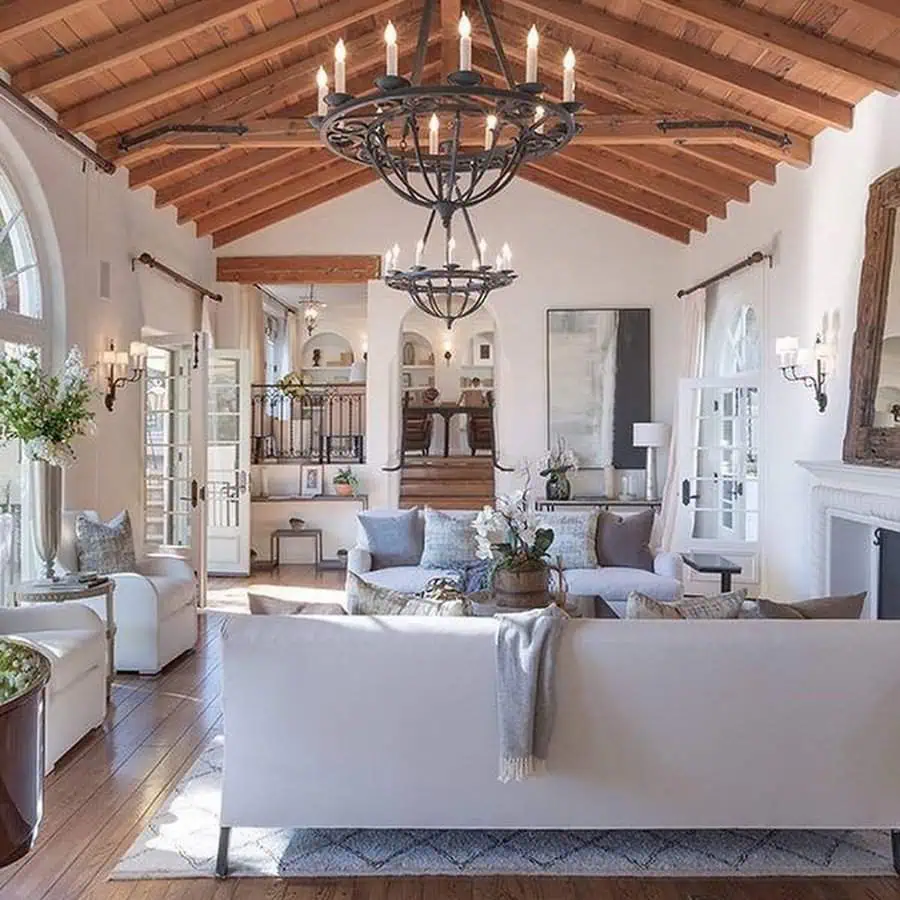 Spanish-style living room with vaulted wooden ceiling, chandeliers, and cozy white furniture.