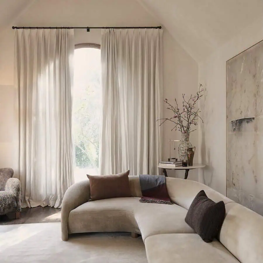 Minimalist Spanish-style living room with arched window, neutral curtains, and a curved sofa.